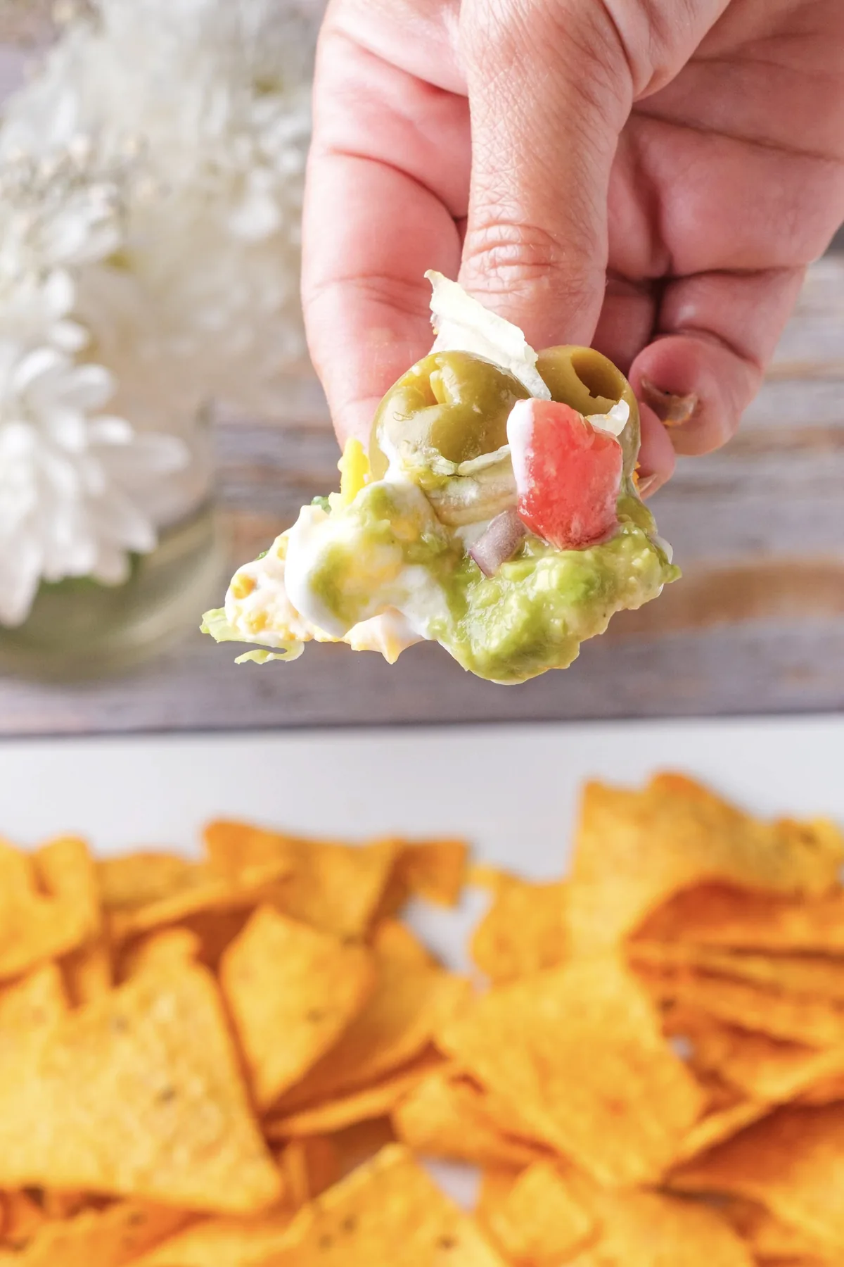 A tortilla chip scooping up hummus, avocado, labneh, tomato, cheese, lettuce and a green olive