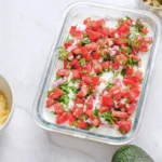 Diced tomato, red onion and chopped arugula scattered over labneh in a glass dish