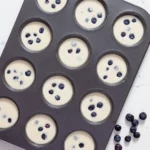 Muffin cups filled with thin popover batter and fresh blueberries before baking.