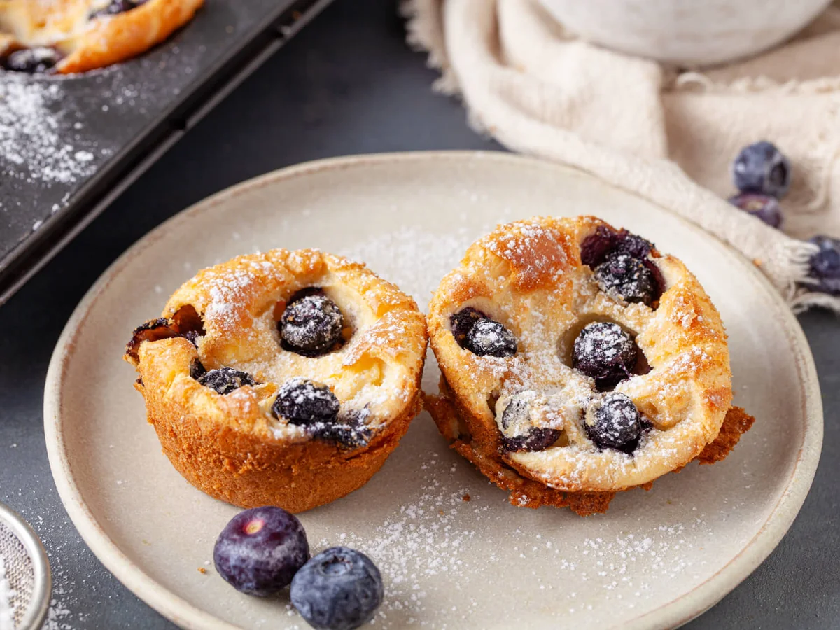 Blueberry Popovers with Lemon in a Muffin Tin Two golden blueberry popovers dusted with powdered sugar on a plate.