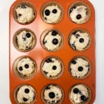 Twelve paper-lined muffin cups filled with blueberry muffin batter before baking.