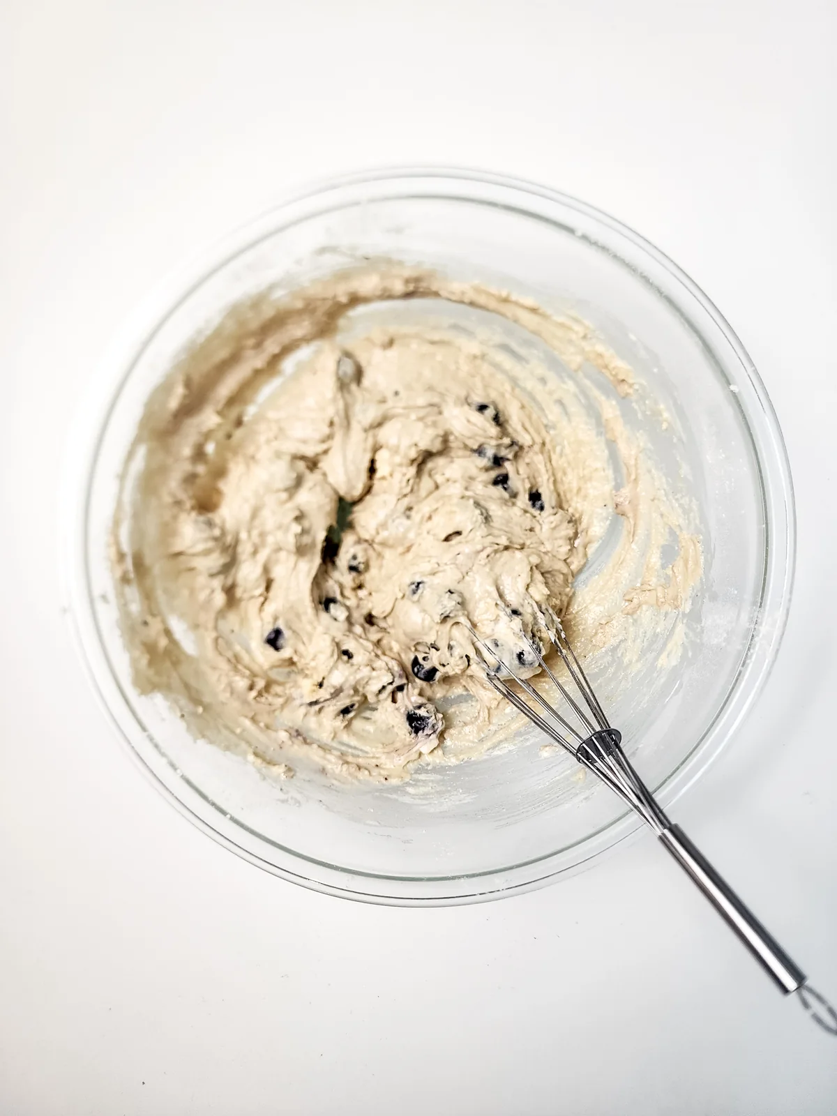 Thick blueberry muffin batter in a mixing bowl with a whisk.
