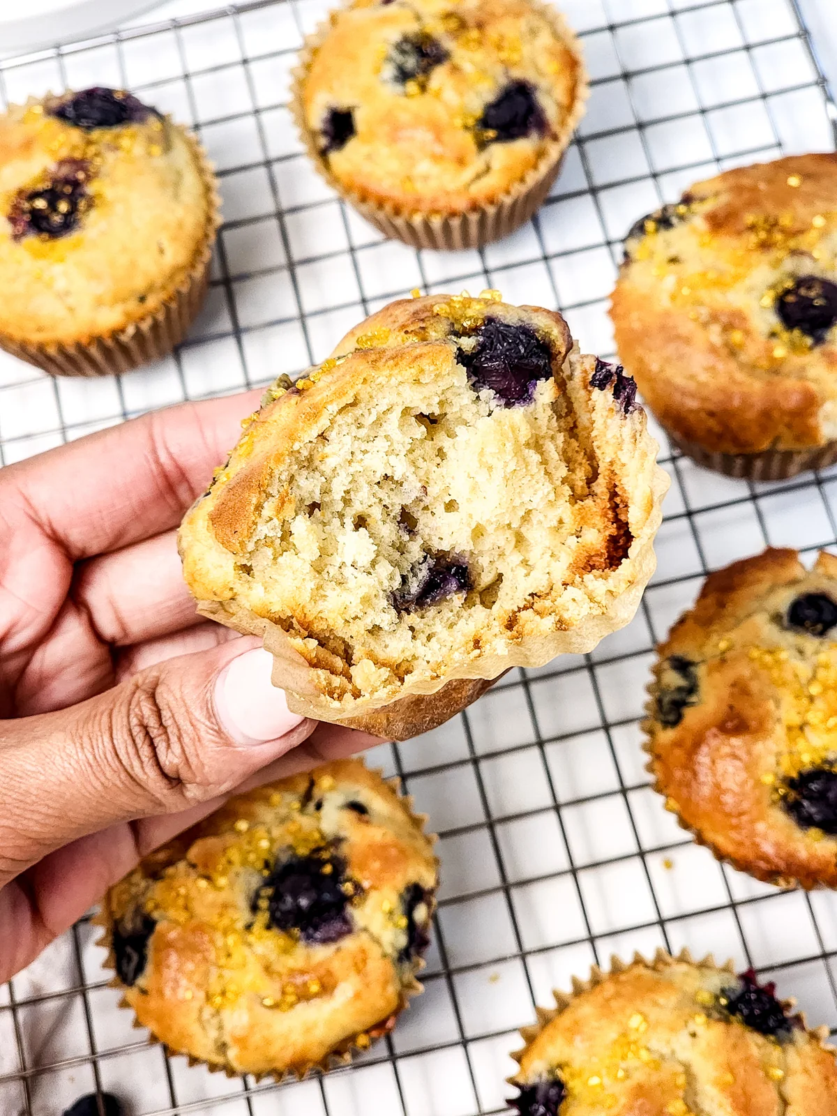 A split blueberry muffin held over a cooling rack to show its tender interior.