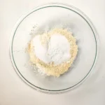 Flour, protein powder, sugar, and leavening in a glass mixing bowl.