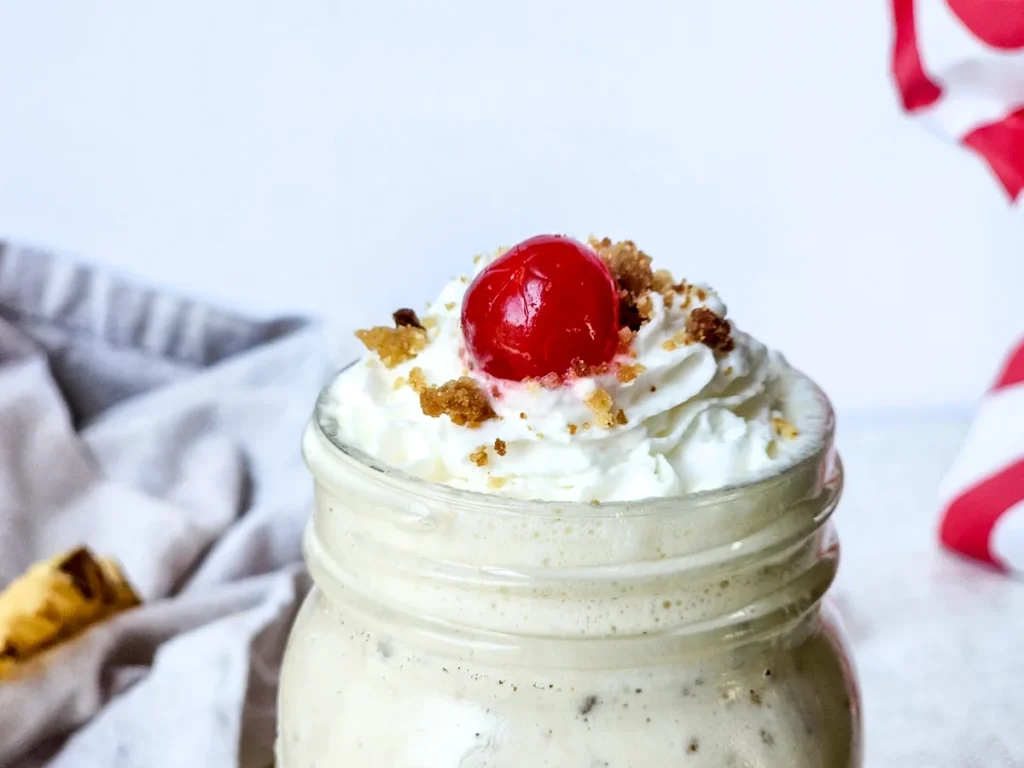 Top view of a caramel crumble milkshake with whipped cream, blondie crumbs, and a cherry.