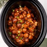 Cooked Hawaiian meatballs in BBQ pineapple sauce in a slow cooker, topped with green onions