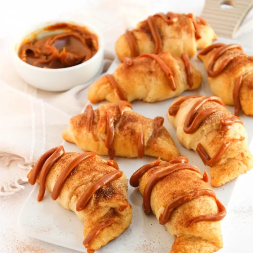 Easy Crescent Roll Churros With Dulce de Leche Crescent roll churros drizzled with dulce de leche on a white serving board