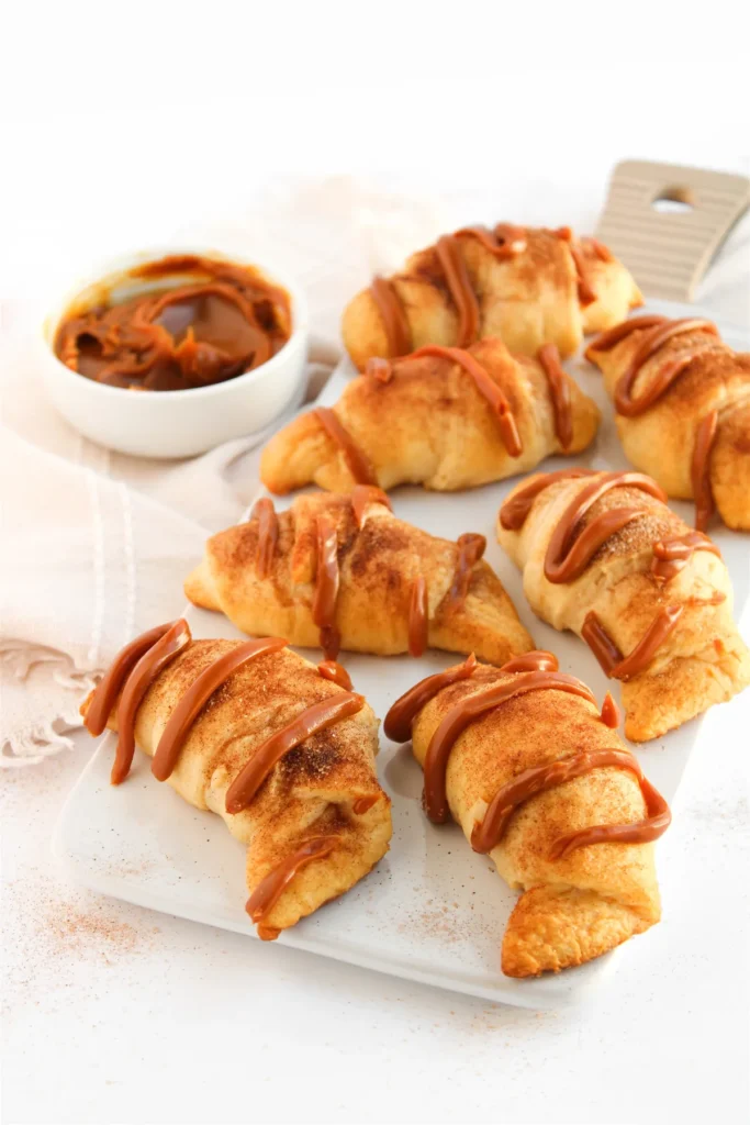 Crescent roll churros drizzled with dulce de leche on a white serving board