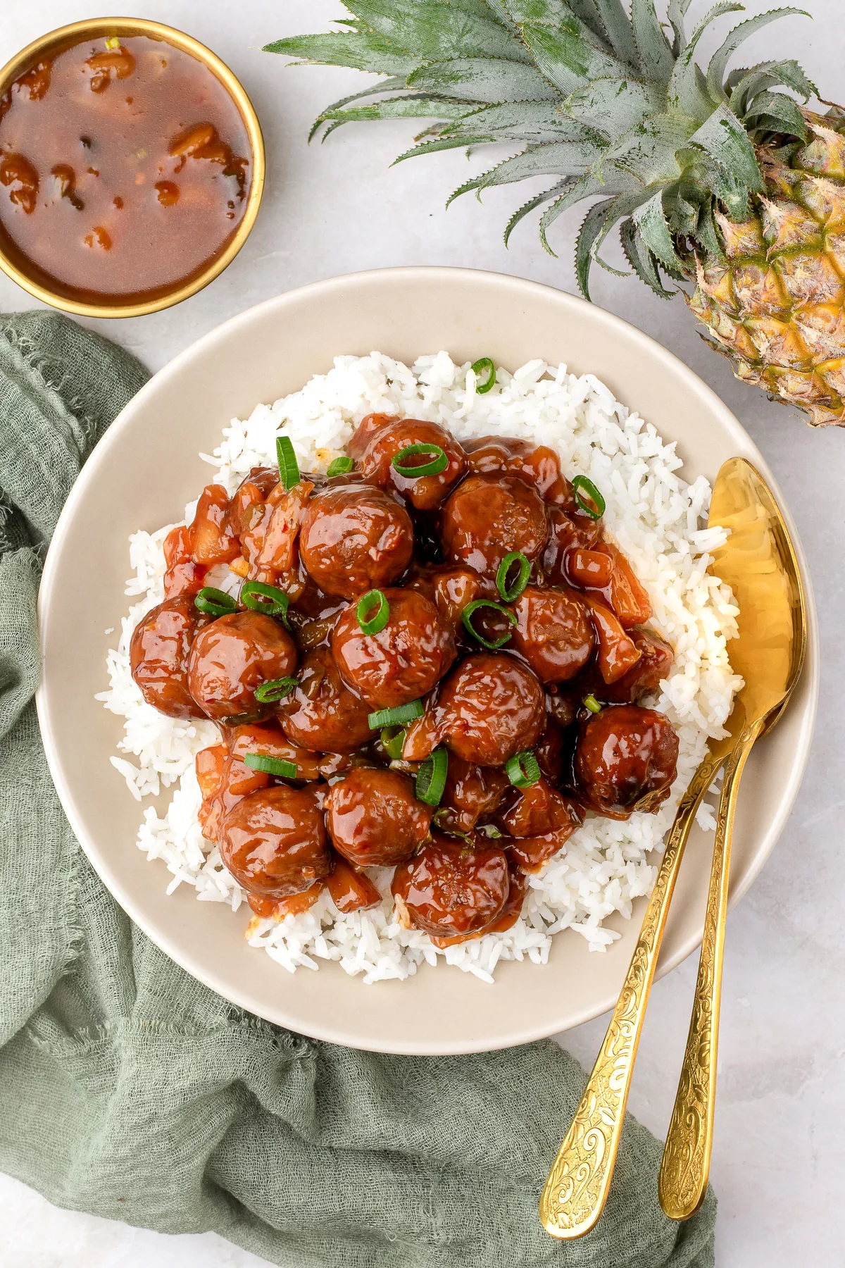 Crockpot Hawaiian meatballs in a glossy BBQ pineapple sauce over white rice, topped with sliced green onions