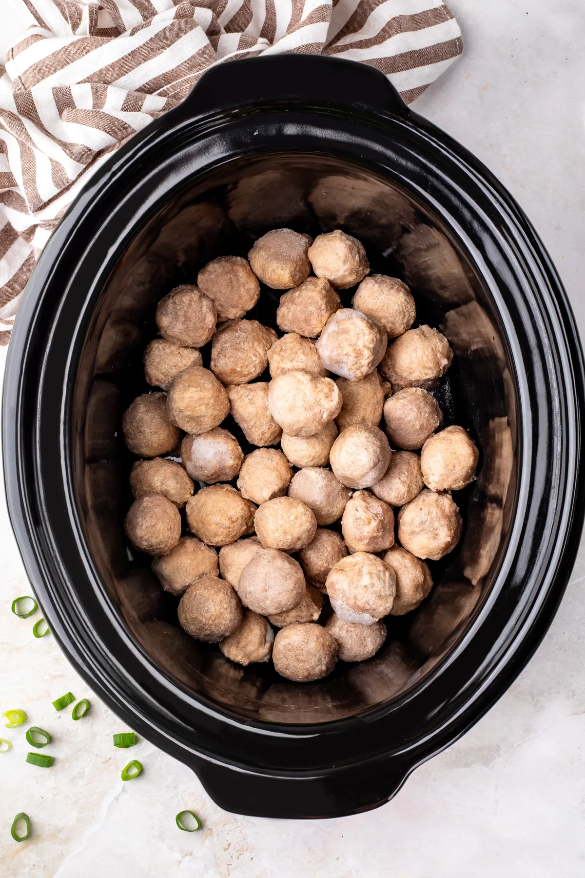 Frozen fully cooked meatballs in a black oval slow cooker