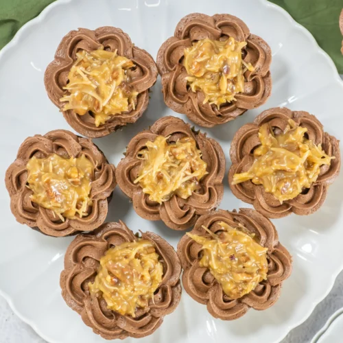 German chocolate cupcakes with coconut-pecan topping arranged on a white platter.