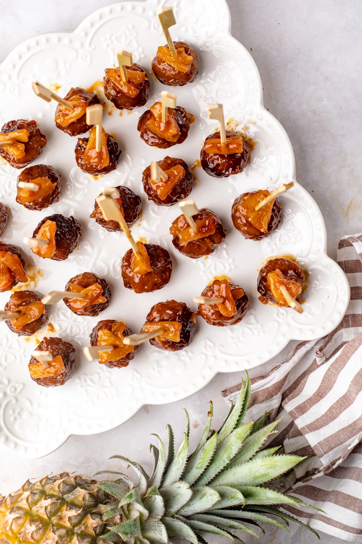 Overhead view of a scalloped white platter filled with Hawaiian meatball appetizer skewers