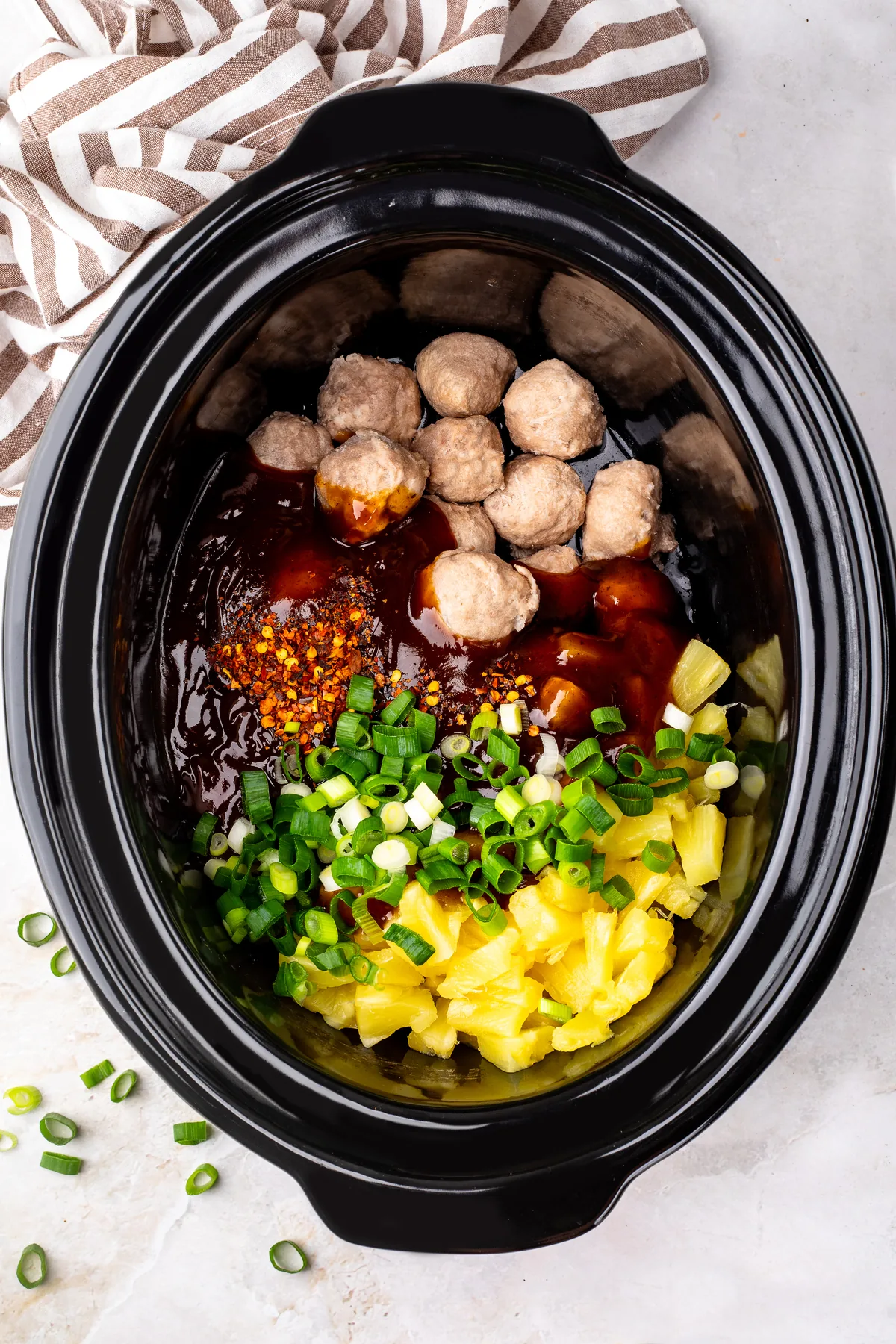 BBQ sauce, red chili flakes, sliced green onions and pineapple chunks on top of frozen meatballs in a slow cooker