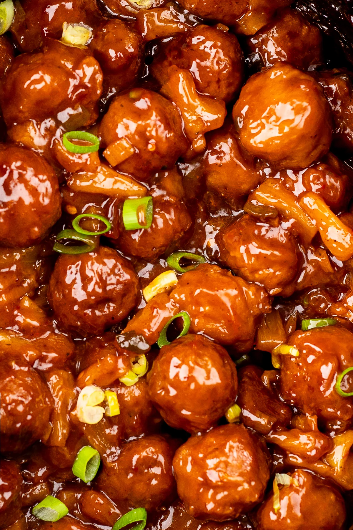 Close-up of cooked meatballs in a sticky BBQ sauce with pineapple and green onions