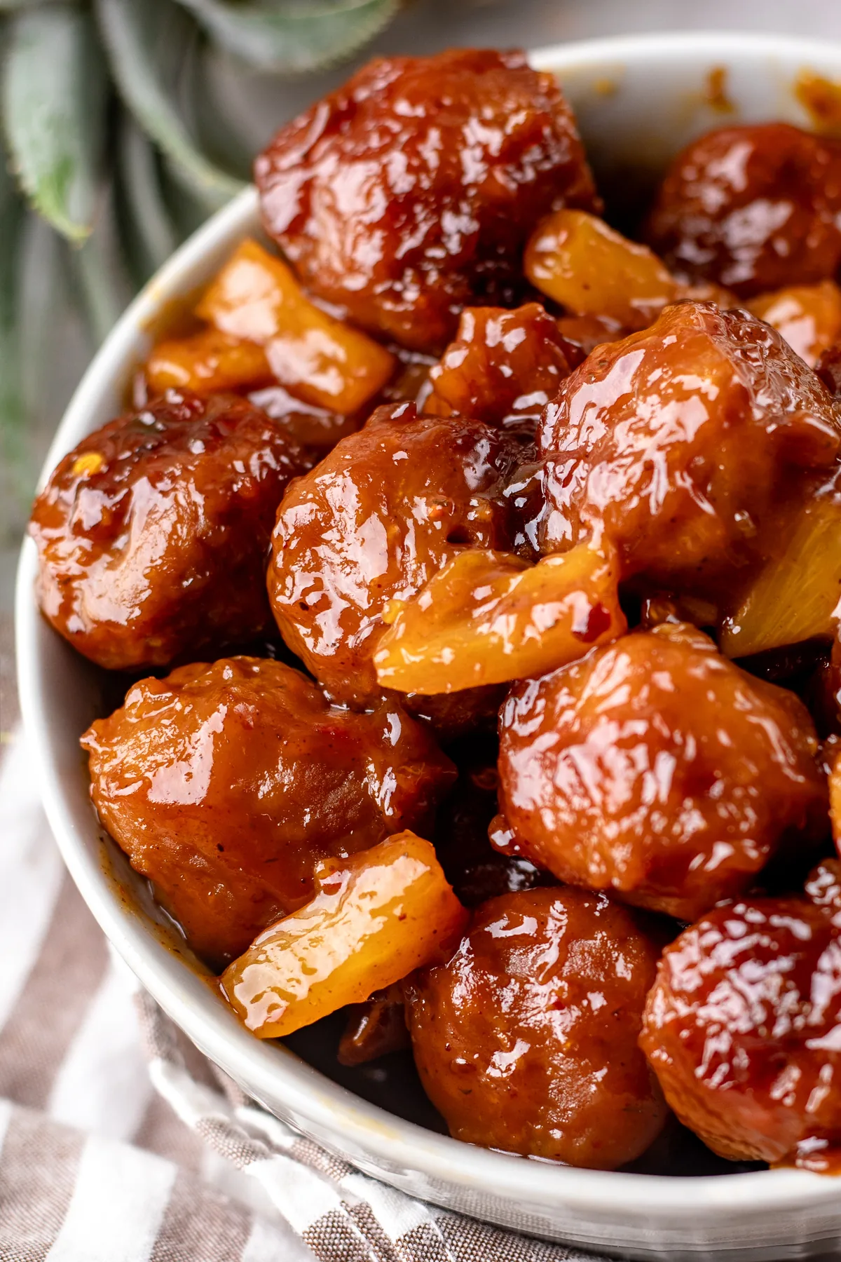 A white bowl of Hawaiian meatballs with pineapple chunks in sticky BBQ sauce