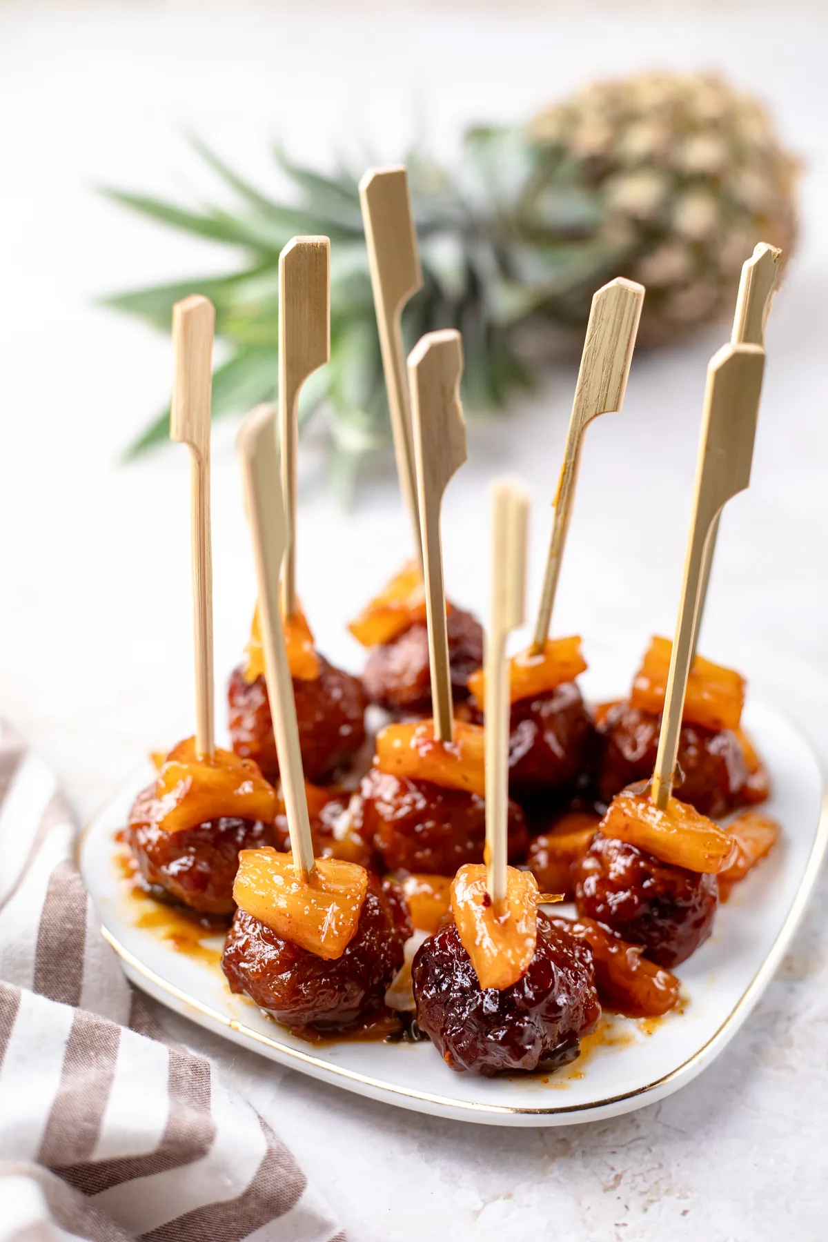 Hawaiian meatballs topped with pineapple chunks on bamboo picks on a white platter