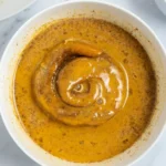 Cinnamon roll half resting in pumpkin custard in a white bowl
