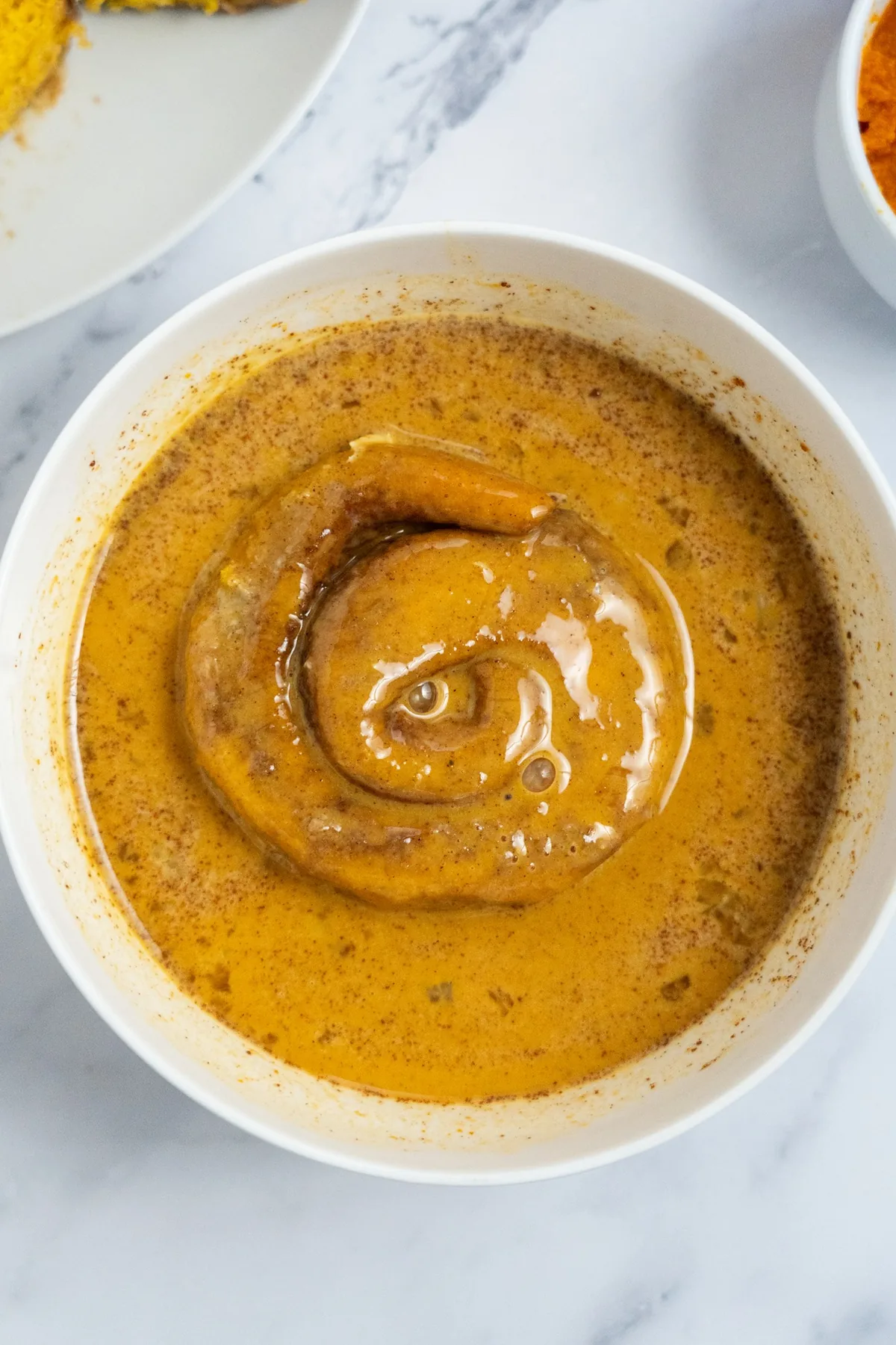 Cinnamon roll half resting in pumpkin custard in a white bowl