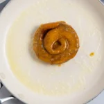 Custard-dipped cinnamon roll half cooking in melted butter in a white skillet