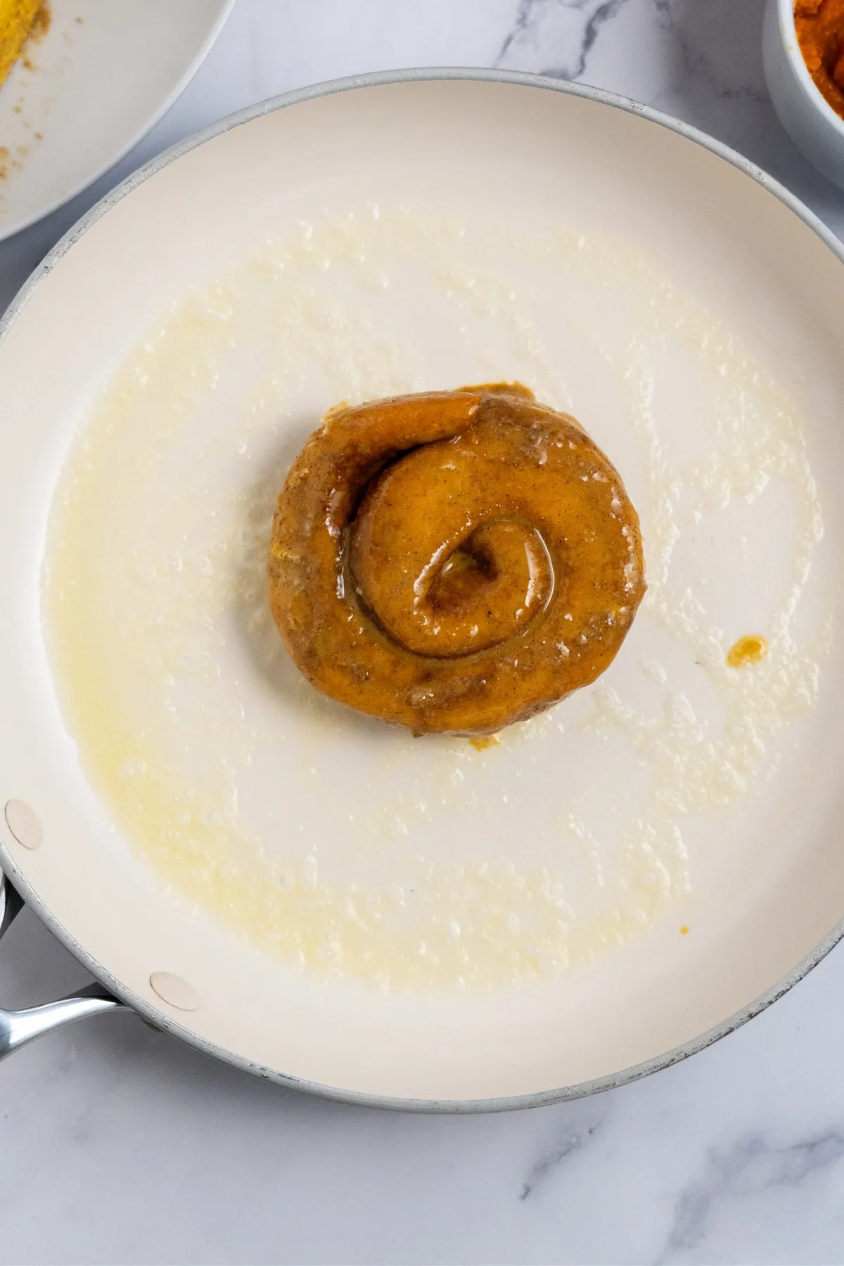 Custard-dipped cinnamon roll half cooking in melted butter in a white skillet