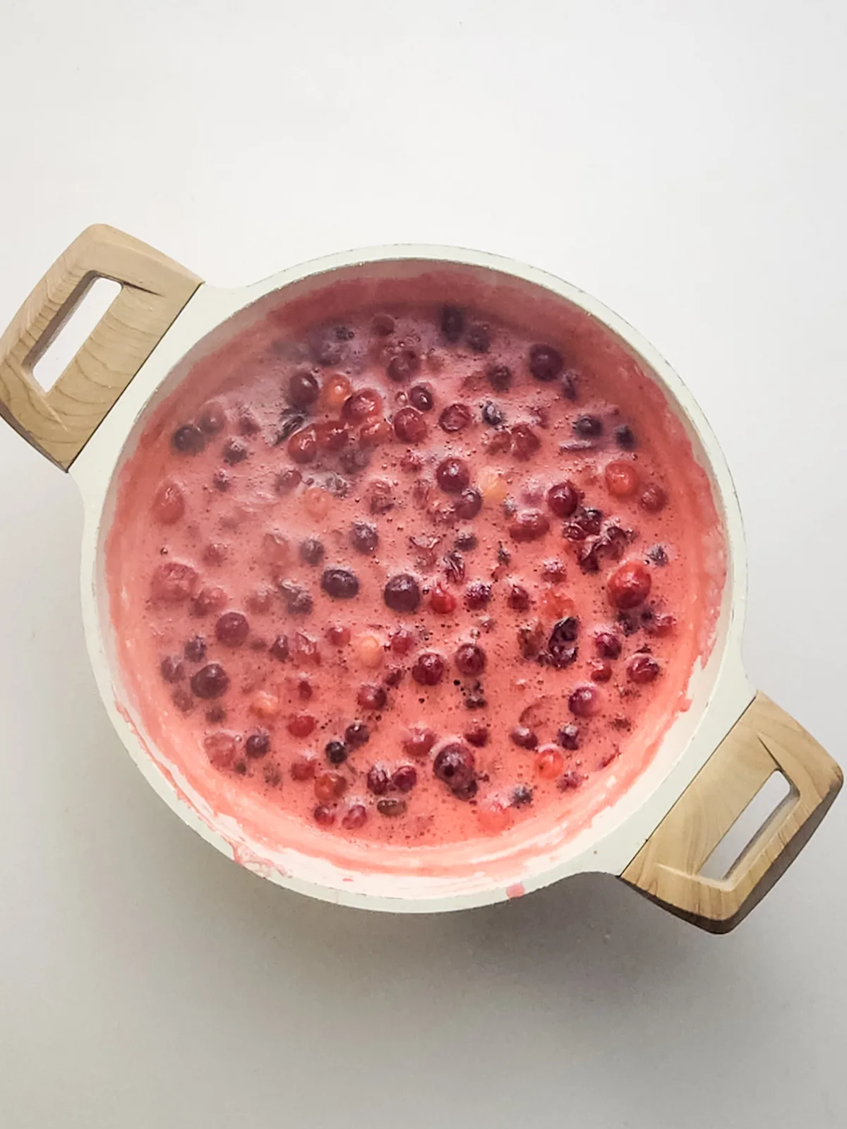 Cranberries simmering in a large pot as they soften and begin to burst.