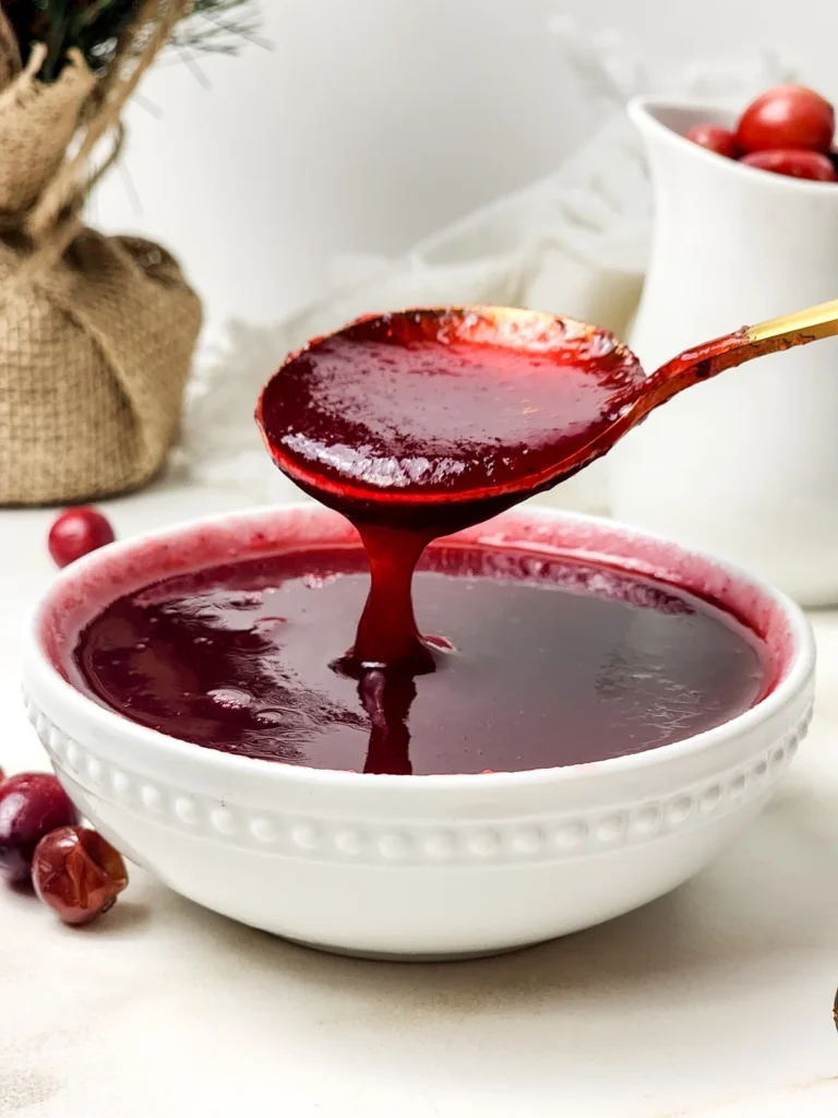 Smooth cranberry sauce flowing from a gold spoon into a white bowl.