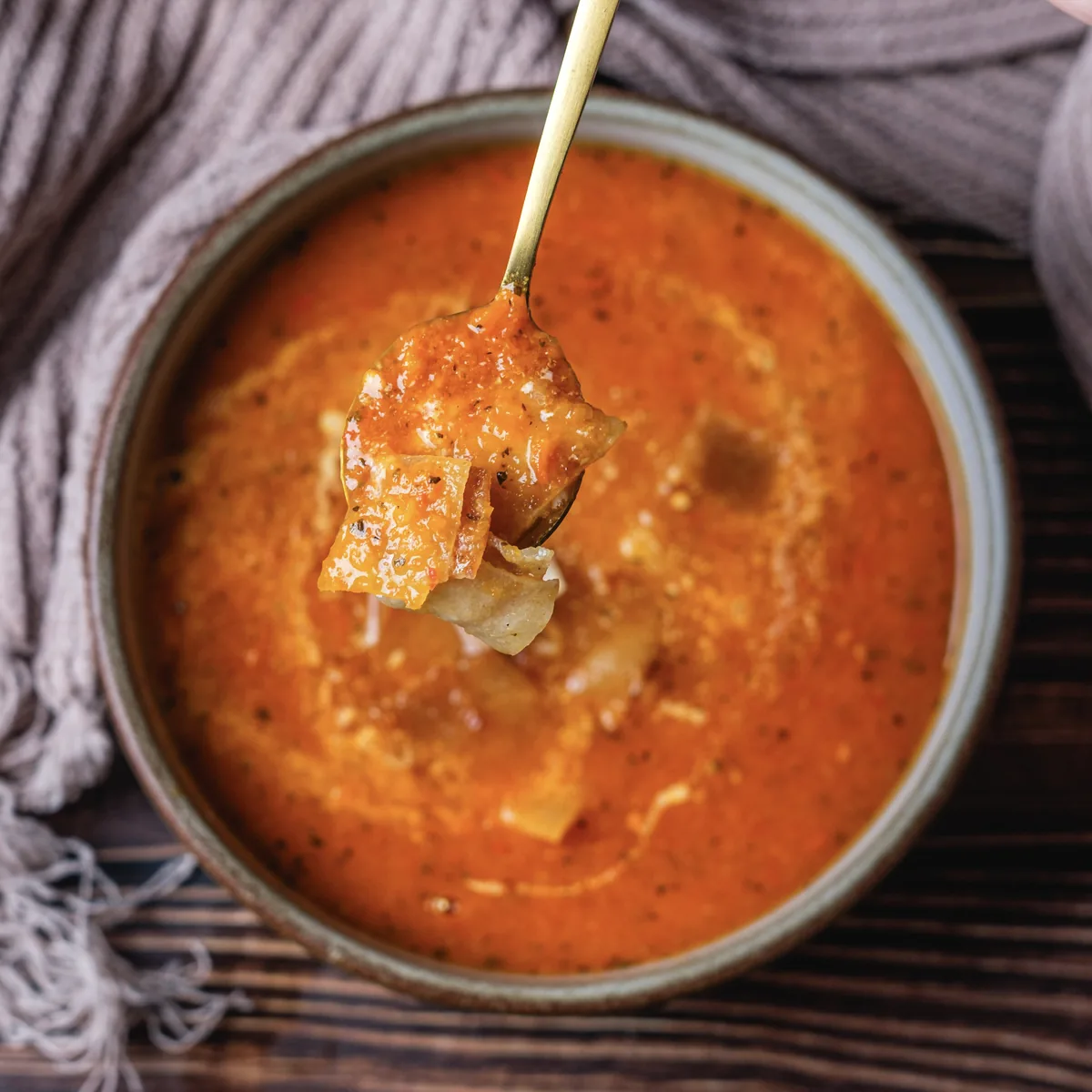 Tomato Bisque Soup With Fresh Tomatoes (Small Batch for Two) A gold spoon lifting a crouton out of a bowl of creamy tomato bisque on a dark wood table