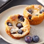 Warm blueberry popovers with powdered sugar and fresh blueberries.