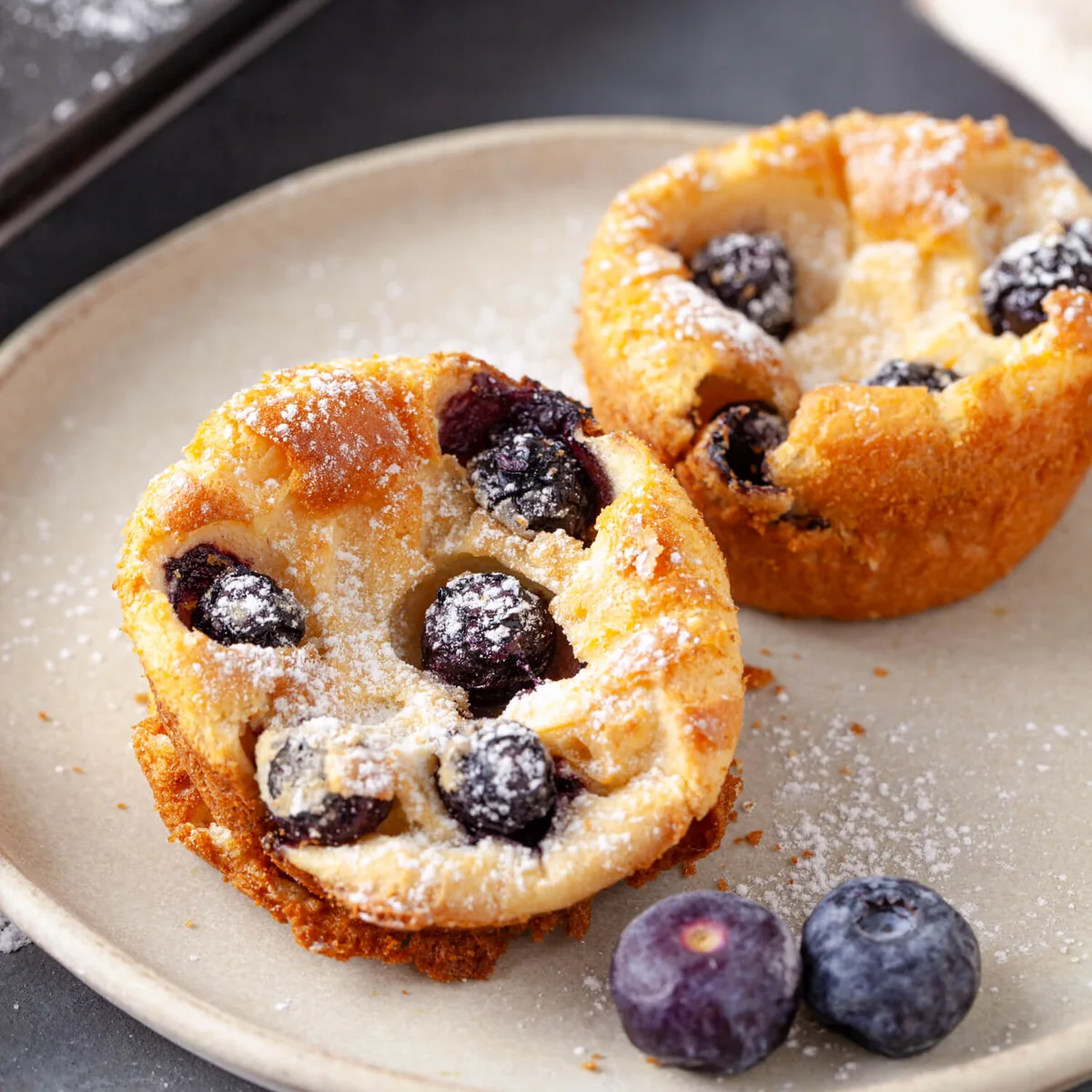 Warm blueberry popovers with powdered sugar and fresh blueberries.